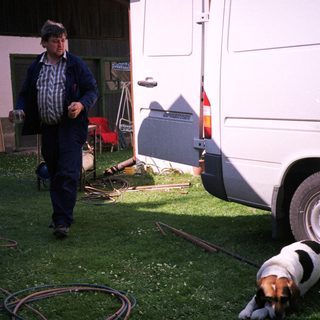 Man washing camper exterior with hose, dog nearby.