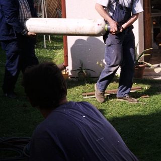 People moving large cylindrical object near camper van.