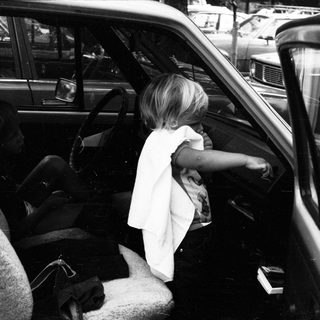 Child sitting in car, leaning out open door.