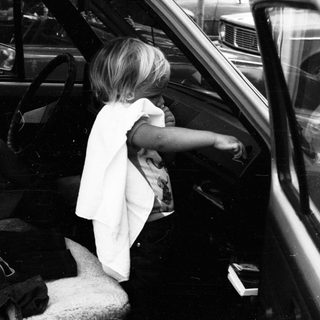 Child sitting in car, leaning out open door.