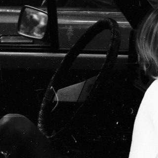 Child sitting in car, leaning out open door.