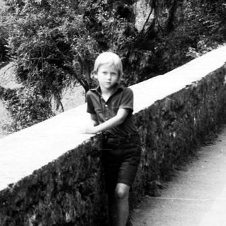Child standing near cliffside castle.