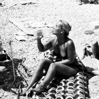 Two women relaxing on beach towels, drinking.