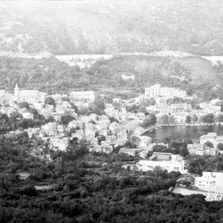 Historic coastal town with hillside buildings and lake.