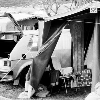 Camping scene with tent and parked camper van.