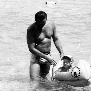 Man assisting child in shallow ocean water.