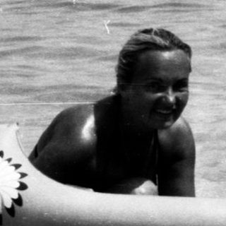 Two people in inflatable raft near water, with motorboats and swimmers in background.