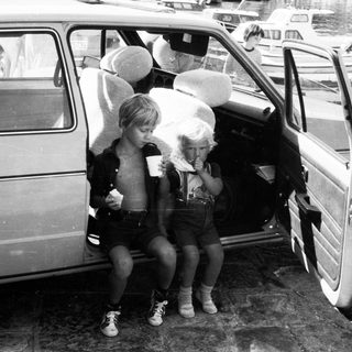 Two children eating ice cream by open car door.