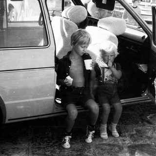 Two children eating ice cream by open car door.