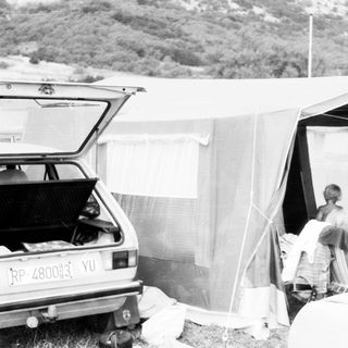 Campsite with open tent, car trunk, and people unpacking.