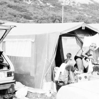 Campsite with open tent, car trunk, and people unpacking.