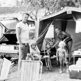 Family camping outdoors near tent with car.