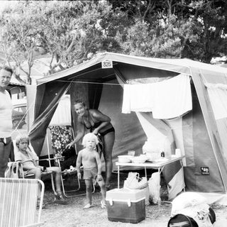 Family camping outdoors near tent with car.