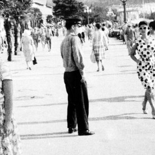 Vintage seaside promenade with palm trees and mid-20th-century attire.