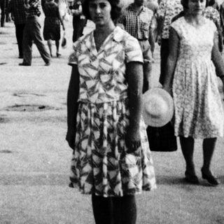 Mid-20th-century seaside promenade with palm trees and people.