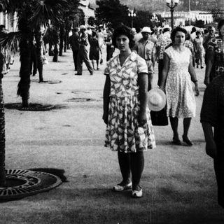 Mid-20th-century seaside promenade with palm trees and people.