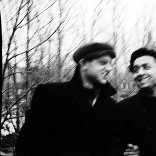 Two men smiling outdoors in vintage-style photograph.