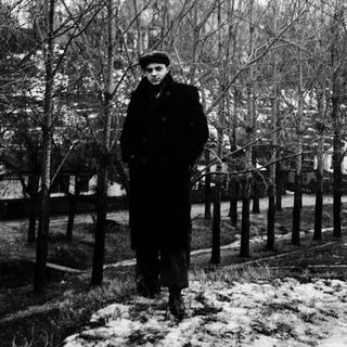 Man in winter coat and cap standing outdoors in snow.