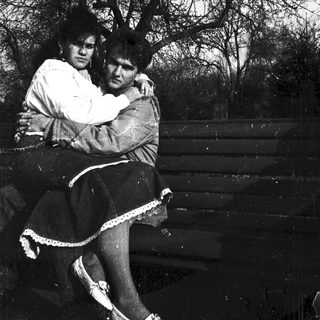 Two people hugging closely outdoors near trees.