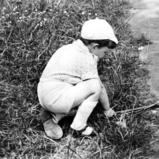 Child squatting by riverbank, wearing cap and shorts.