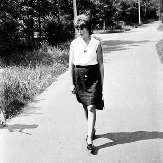 A woman walks alone on a sunny road.