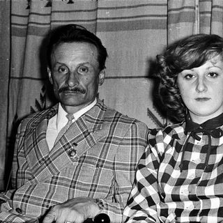 Two individuals in 1970s-style plaid clothing posing indoors.