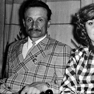 Two individuals in 1970s-style plaid clothing posing indoors.