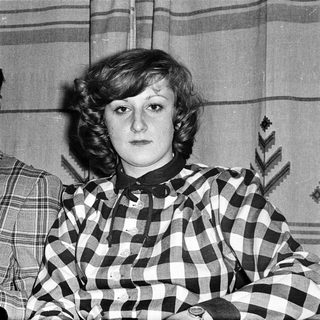 Two individuals in 1970s-style plaid clothing posing indoors.