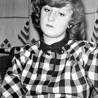 Young woman wearing plaid shirt, seated indoors.
