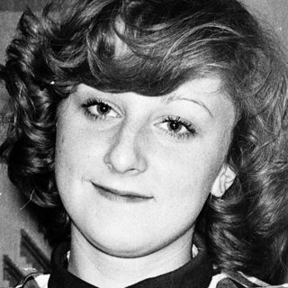 Young woman wearing plaid shirt, smiling slightly.