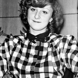 Young woman wearing plaid shirt, smiling slightly.
