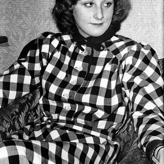 Young woman wearing plaid shirt, seated indoors.