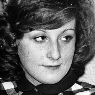 Young woman wearing plaid shirt, seated indoors.