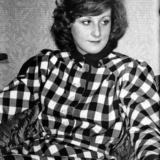 Young woman wearing plaid shirt, seated indoors.