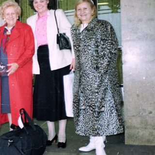 Group of five adults posing with luggage at travel entrance.