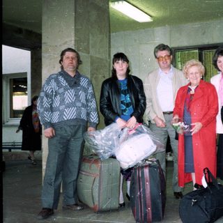 Group of five adults posing with luggage at travel entrance.