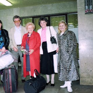 Group of five adults posing with luggage at travel entrance.