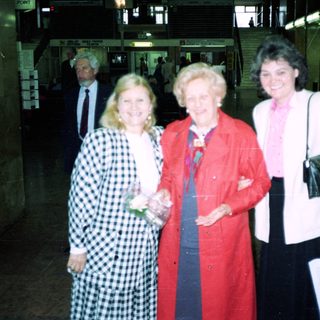 Three women posing indoors near airport baggage claim.