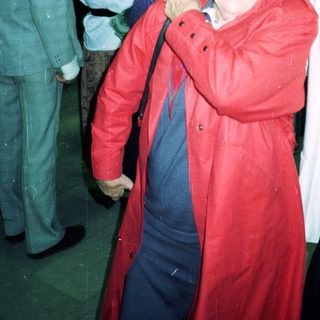 Smiling elderly woman in red coat at indoor event.