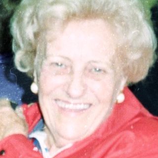 Smiling elderly woman in red coat at indoor event.