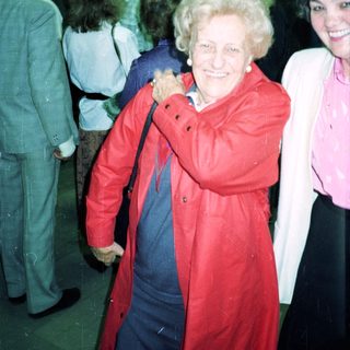 Smiling elderly woman in red coat at indoor event.