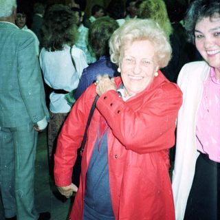 Smiling elderly woman in red coat at indoor event.