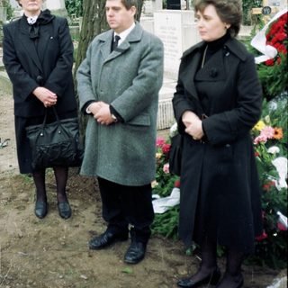 Three people standing solemnly at a gravesite.