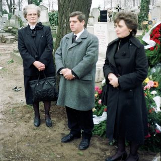 Three people standing solemnly at a gravesite.