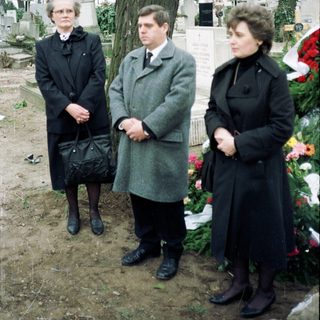 Three people standing solemnly at a gravesite.