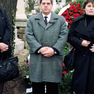 Three people standing at a gravesite during a funeral.