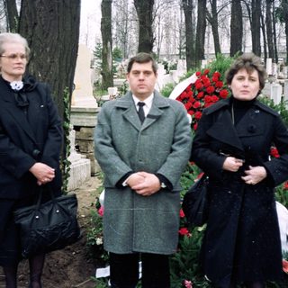 Three people standing at a gravesite during a funeral.