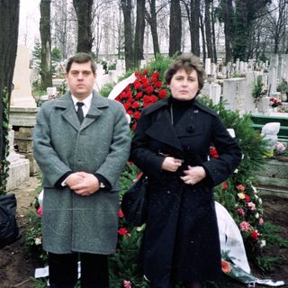 Three people standing at a gravesite during a funeral.