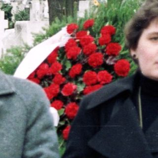 Three people standing at a gravesite during a funeral.