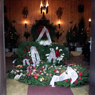 Memorial wreaths and floral tributes in a solemn indoor setting.